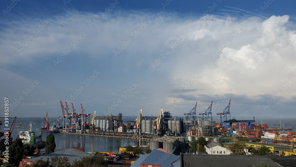 Industrial port landscape with cargo cranes and grain elevators under cloudscape