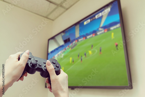 woman playing video game. Hands holding console controller. Football or soccer game on the television. Widescreen tv stands on commode.