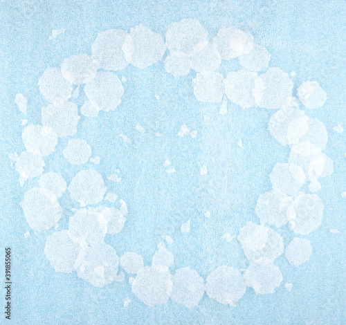 White round plastic foam sheet pieces on blue background. Winter snowfall concept. Frame of torn foam polyethylene transparent pieces as snowflakes.
