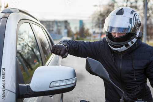 Obraz na płótnie Motorcyclist beat side-view mirror of car with a fist, conflict is on the road