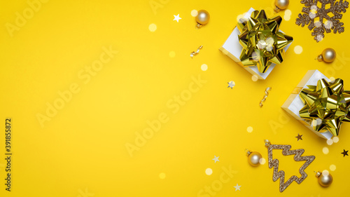Happy xmas. White gift box with golden color ribbon  New Year balls and sparkling lights in Christmas composition on dark yellow background for greeting card. Copy space. Winter holidays  New Year.