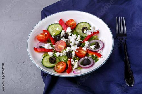 Light plate of Greek salad on a blue napkin on a concrete background.