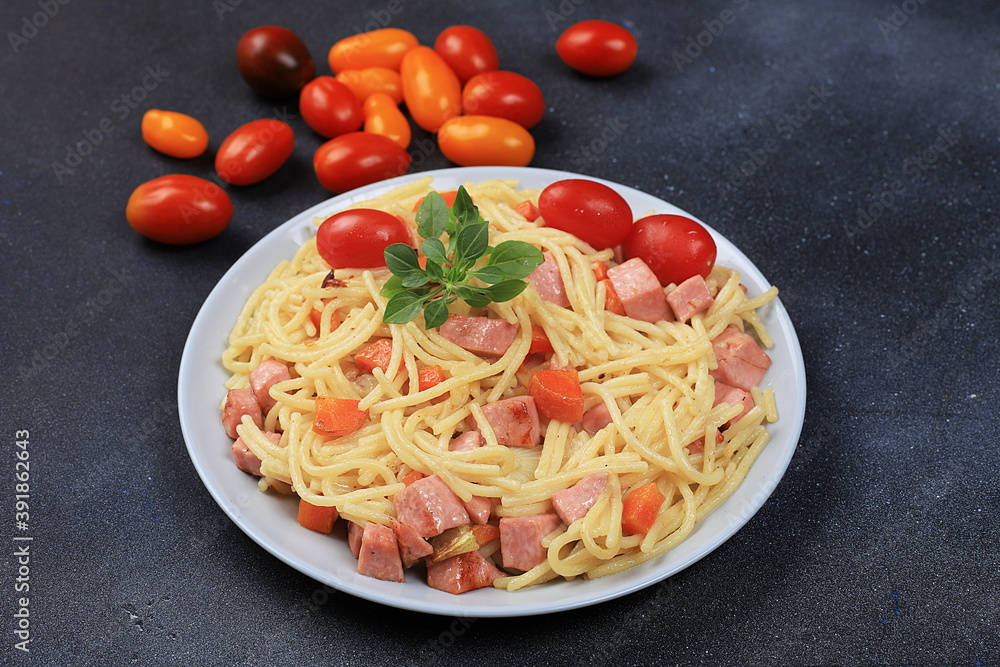 Italian spaghetti pasta with cherry tomatoes, tomato sauce, basil, fried carrots and sausage on a dark table, top view, selective focus