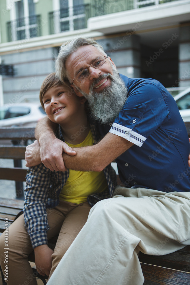 Fototapeta premium Vertical shot of a happy elderly man smiling to the camera, hugging his grandson