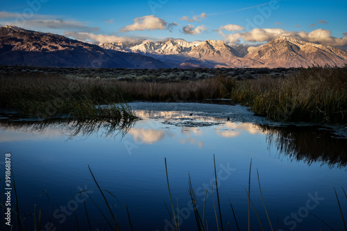 First morning light illuminates mountains with darker valley wetlands grasses reflection in water