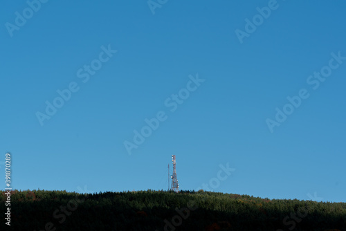 A telecommunications tower on top of forest hill with clear blue sky lots of copy space for advert text clean sharp colors and focus