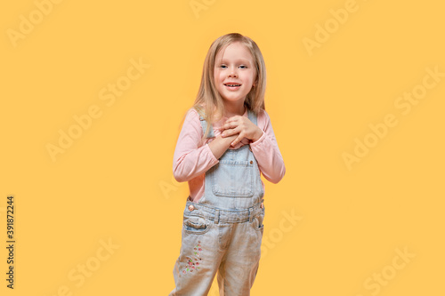 Beautiful cute blonde girl in casual clothes looks at the camera. Yellow isolated background.