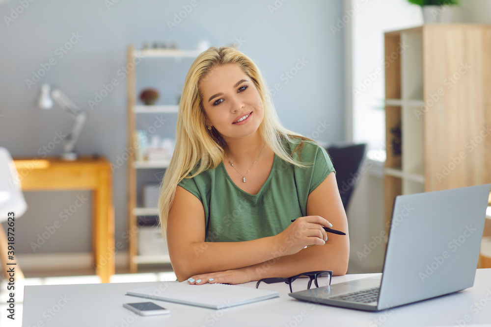 Smiling woman working online with notebook and looking at camera at home or modern office Smiling woman working online with notebook and looking at camera at home or modern office