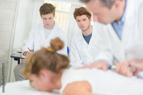 Students watching doctor working on patient s back