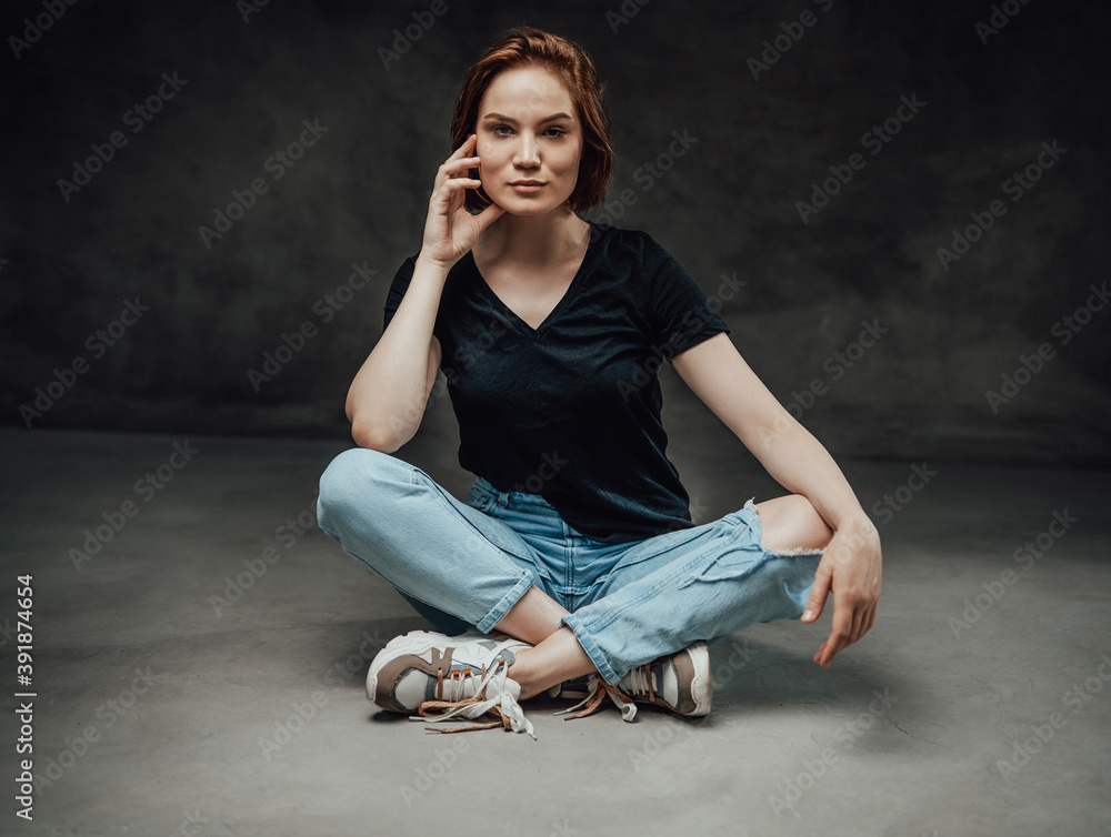 Relaxed and cheerful female model with short haircut in black shirt poses in dark background with hand near her face. Relaxed and cheerful female model with short haircut in black shirt poses in dark background with hand near her face.