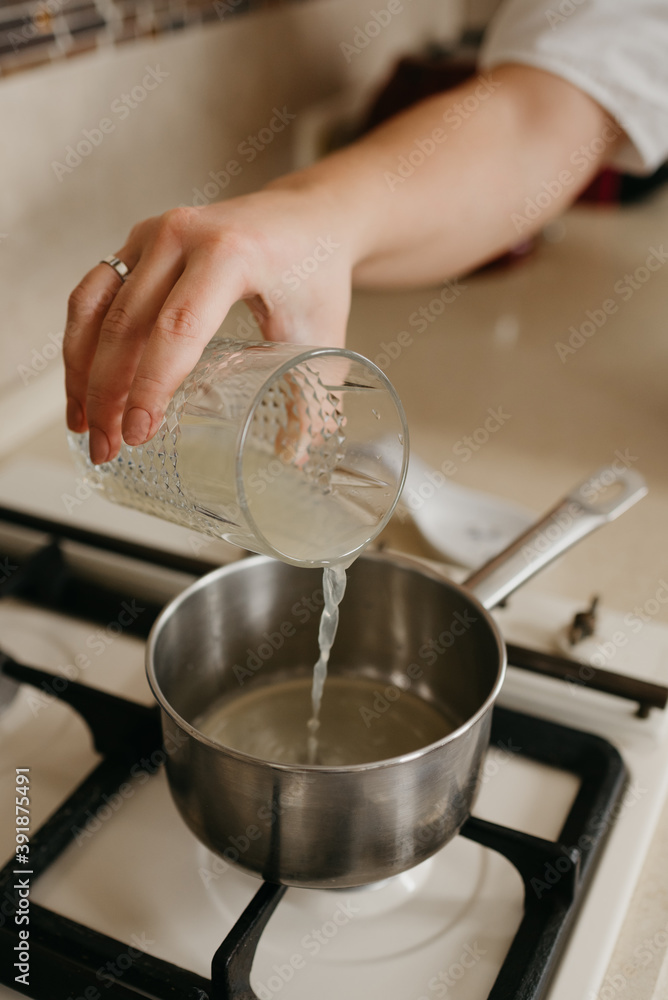A hand of a woman who is pouring fresh lemon juice from the glass to the saucepan on the gas stove A hand of a woman who is pouring fresh lemon juice from the glass to the saucepan on the gas stove