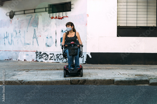 Young woman in electric scooter for disabled. She cannot cross the street because there is not ramp. Grunge wall at the background. Disgusted invalid girl.