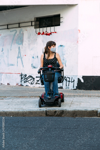 Young woman in electric scooter for disabled. She cannot cross the street because there is not ramp. Grunge wall at the background. Disgusted invalid girl.