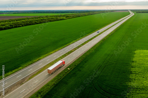 red truck driving on asphalt road along the green fields. seen from the air. Aerial view landscape. drone photography. cargo delivery