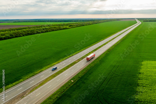 blue car and red truck driving on asphalt road along the green fields. seen from the air. Aerial view landscape. drone photography.  cargo delivery © drotik