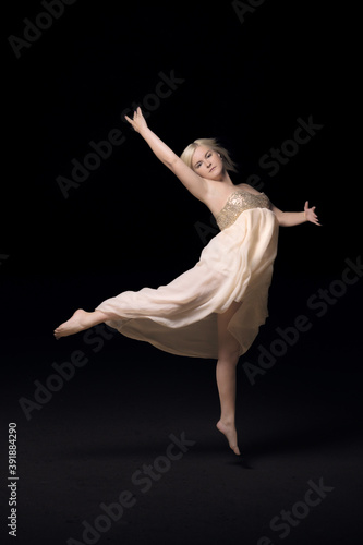 White girl dancing ballet on a black background. A young woman of European appearance froze in a jump. Ballet dance in white dress on black background. Ballerina soars in a jump
