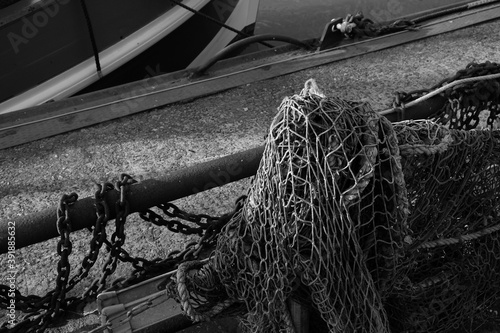 Fischernetz mit alter Kette im Sonnenschein an einer Anlegestelle im Hafen von Neuharlingersiel an der Küste der Nordsee bei Esens in Ostfriesland in Niedersachsen in neorealistischem Schwarzweiß photo