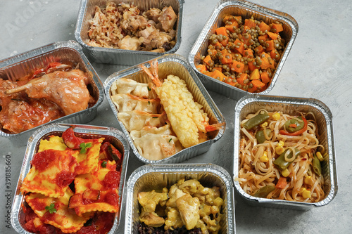 Takeout coronavirus food. Different aluminium lunch box with ravioli, curry chicken rice, gyoza tempura, noodles vegetables, lentils with pumpkin. covid-19 takeaway food delivery. 