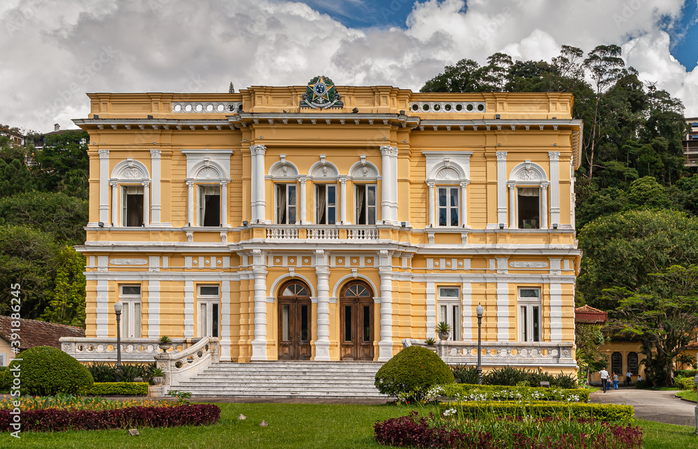 Petropolis, Brazil - December 23, 2008: Closeup of yellow front facade with white frames of Palacio Rio Negri, or black river Palace in its green park under blue cloudscape