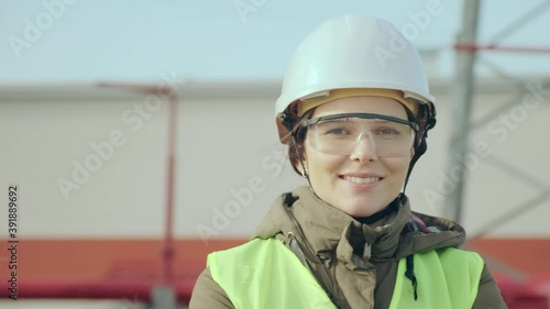 Nice skilled construction engineer woman in special transparent goggles and helmet smiles against transformer substation closeup