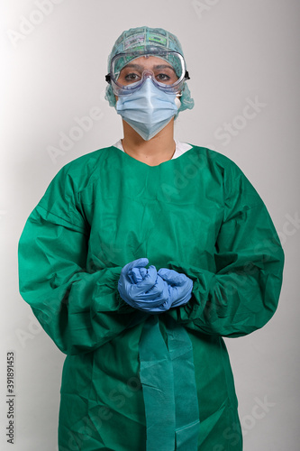 Enfermera protegida con traje (EPI), gafas y mascarilla, mira hacia el frente con las dos manos juntas