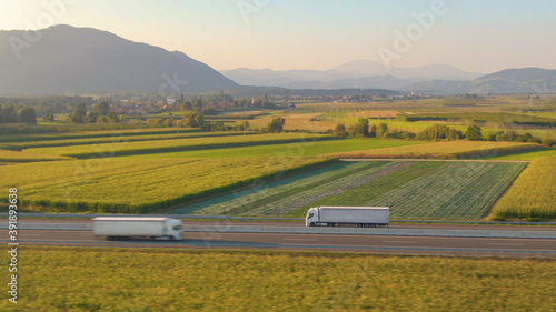 AERIAL: Flying along a white semi truck hauling freight down a scenic highway.