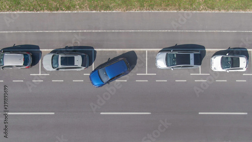 TOP DOWN: Flying above a shiny blue car driving out of a roadside parking space.