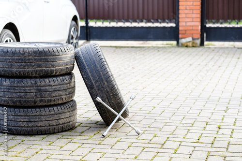 The wrench rests on the foot of the car wheels. An unknown white car on a blurred background. The concept of seasonal replacement of summer car tires with winter tires. Autumn day.