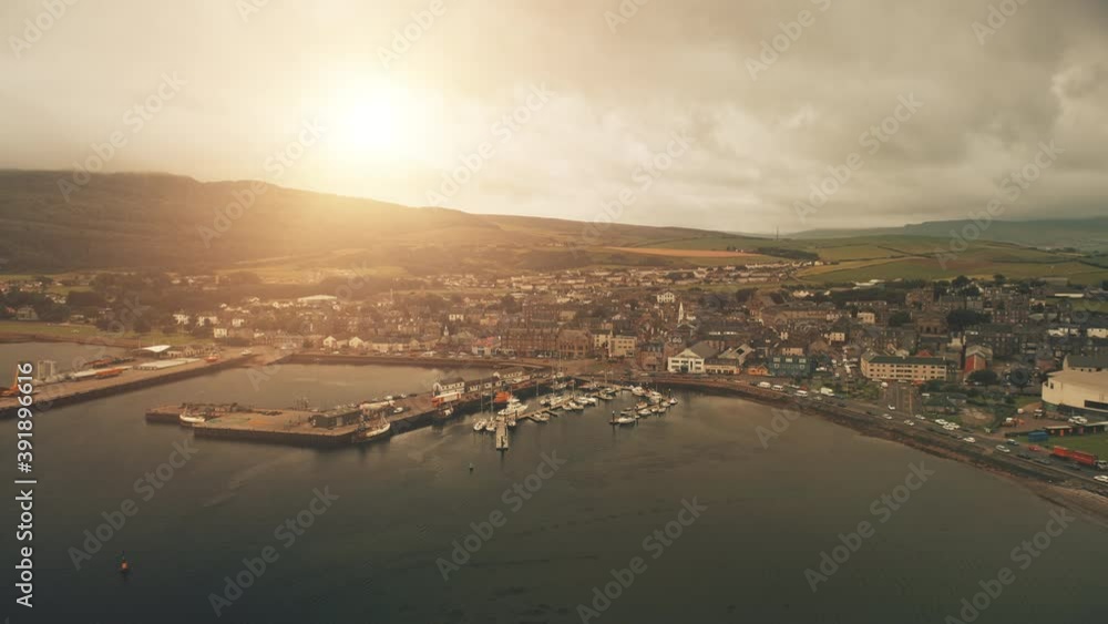 Pier town citycsape with historic buildings at ocean bay aerial. Sun shine over ships, yachts at marina wharf. Streets, road with cars, trucks. Green hill, valley at Campbeltown city, Scotland, Europe Pier town citycsape with historic buildings at ocean bay aerial. Sun shine over ships, yachts at marina wharf. Streets, road with cars, trucks. Green hill, valley at Campbeltown city, Scotland, Europe