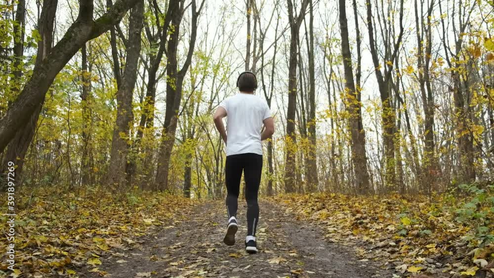 A young bearded man runs in the park and listens to music. Sports and health in the autumn park A young bearded man runs in the park and listens to music. Sports and health in the autumn park