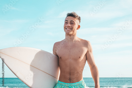 portrait of handsome young man walking on the beach with his surfboard ready to ride waves and go surfing in his vacation time