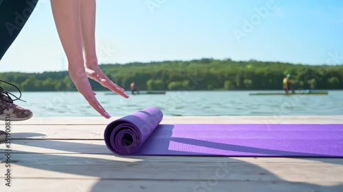 Woman hands rolling purple yoga exercise mat and getting prepared for practice. Team of sports men kayaking on the lake in background. Sunny day. Slow motion. Chisinau, Moldova photo