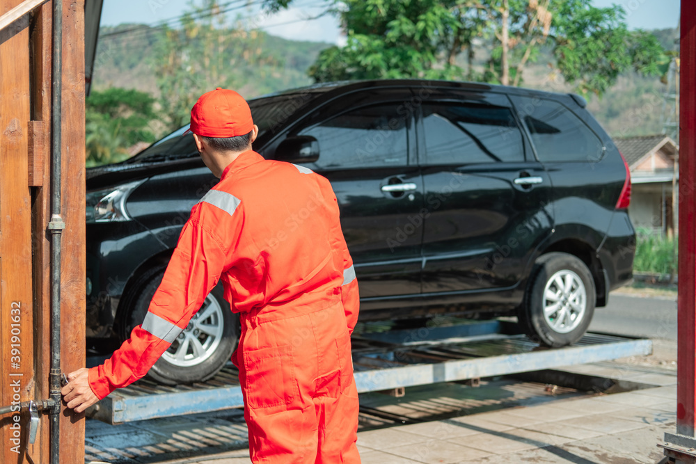 male car cleaner wearing the red uniform and the hat set the faucet to raise the car hydraulics in the car wash male car cleaner wearing the red uniform and the hat set the faucet to raise the car hydraulics in the car wash
