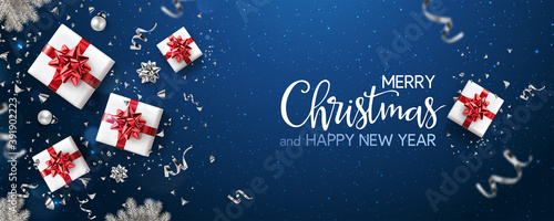 Merry Christmas and New Year text on blue holiday background with red gift boxes, silver fir branches, ribbons, decoration, sparkles, confetti, bokeh, light. Xmas card. Vector Illustration