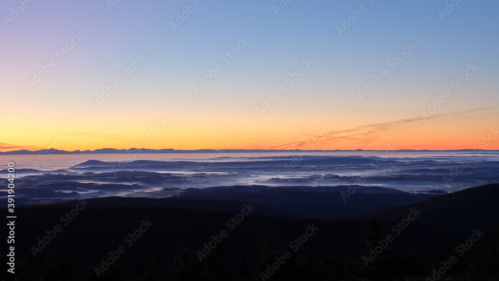 Morning mist and clouds in a valley on an inversion day during sunrise with long mountain ridge on the horizon.