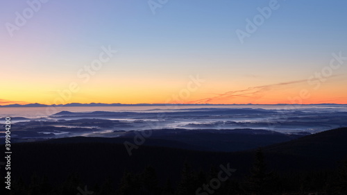 Morning mist and clouds in a valley on an inversion day during sunrise with long mountain ridge on the horizon.