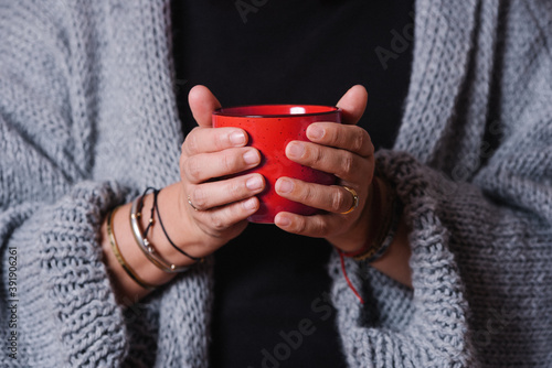 Closeup of a woman's hands with a red mug. Woman warming her hands with a cup of coffee