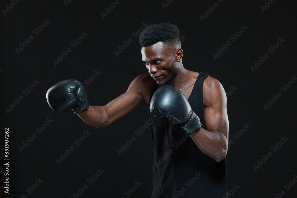Young African American Boxer wearing gloves is posing isolated on a dark background