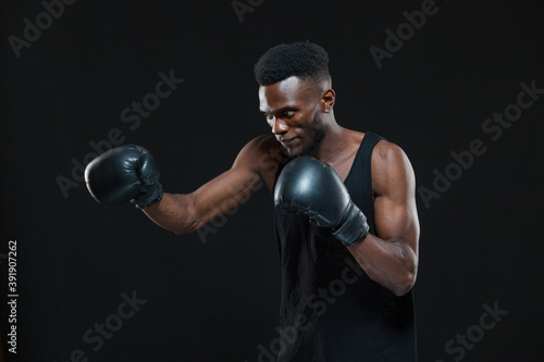 Young African American Boxer wearing gloves is posing isolated on a dark background © satyrenko
