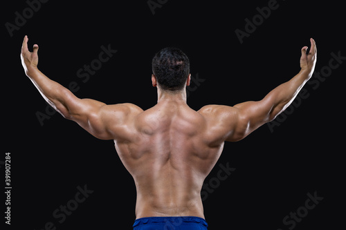 Back view of an attractive sportsman standing with raised arms and showing his muscles isolated on black background