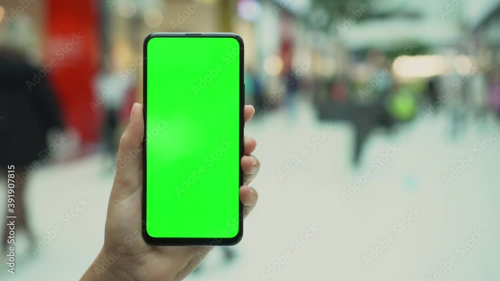 Shopping center. Department store. Mall. Back view of brunette holding chroma key green screen smartphone watching content. Shopping online. Gadgets and contemporary people concept. Shopping center. Department store. Mall. Back view of brunette holding chroma key green screen smartphone watching content. Shopping online. Gadgets and contemporary people concept.
