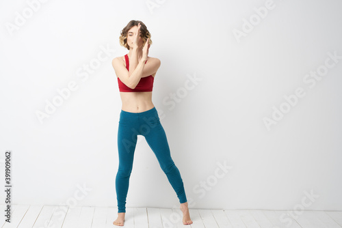 sports woman in a bright room doing yoga in full growth blue leggings and a red tank top © SHOTPRIME STUDIO