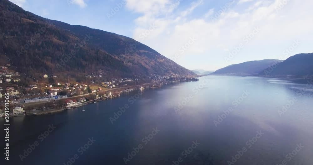 Drone shot flying over a beautiful ice lake and village with grass field in the snow mountains of Austria during winter with mountains and fall forest trees on cloudy day 4k go pro Drone shot flying over a beautiful ice lake and village with grass field in the snow mountains of Austria during winter with mountains and fall forest trees on cloudy day 4k go pro