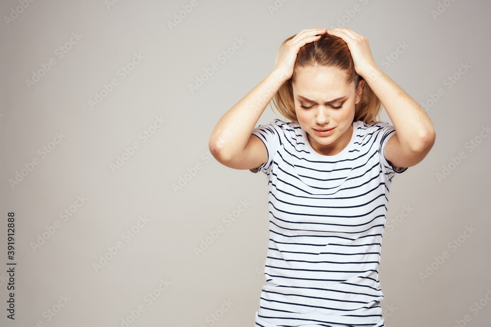 A woman in a striped T-shirt holds her hands in front of her emotions displeasure light background A woman in a striped T-shirt holds her hands in front of her emotions displeasure light background