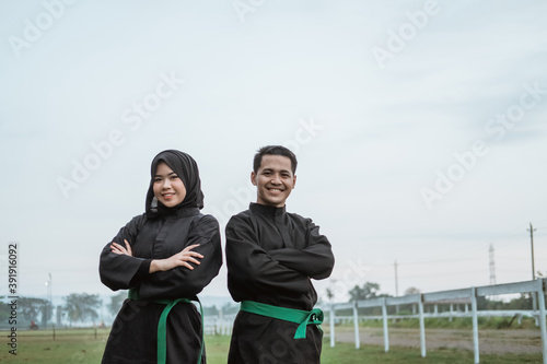 The two Asian fighters wearing pencak silat uniforms with crossed hands in the outdoor background photo