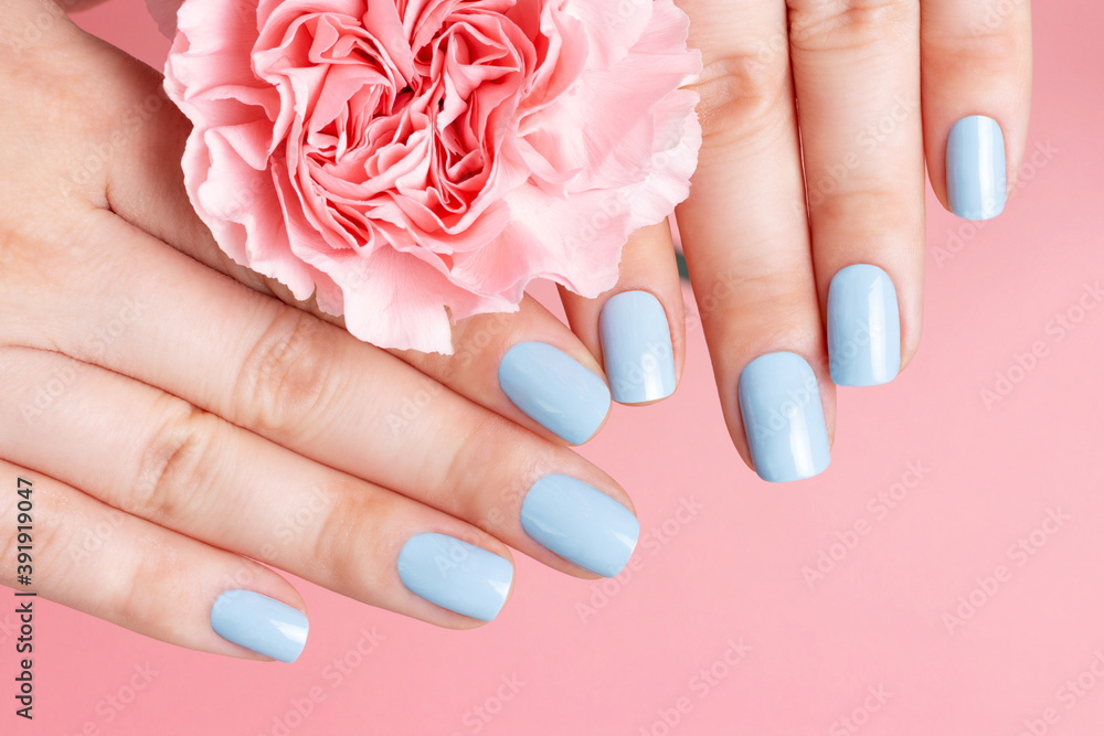 Female hands with manicure on flower on pink background, top view