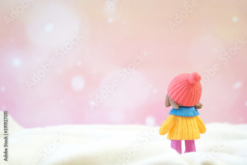 Little girl toy wear sweater and hat stand back on pink bokeh background. Winter season. Merry christmas and happy new year. Copy space.