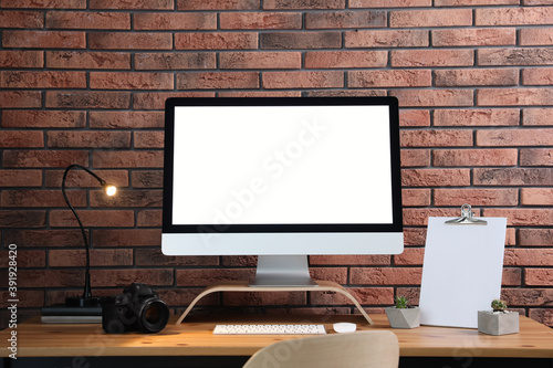 Comfortable workplace with modern computer on wooden table near brick wall. Space for text