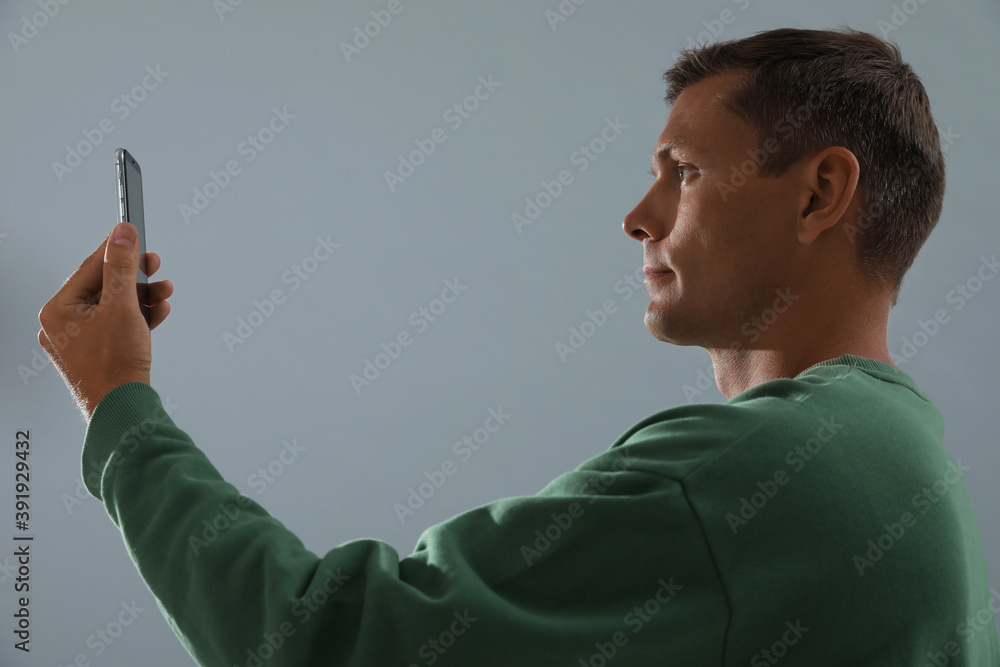 Man unlocking smartphone with facial scanner on grey background. Biometric verification Man unlocking smartphone with facial scanner on grey background. Biometric verification