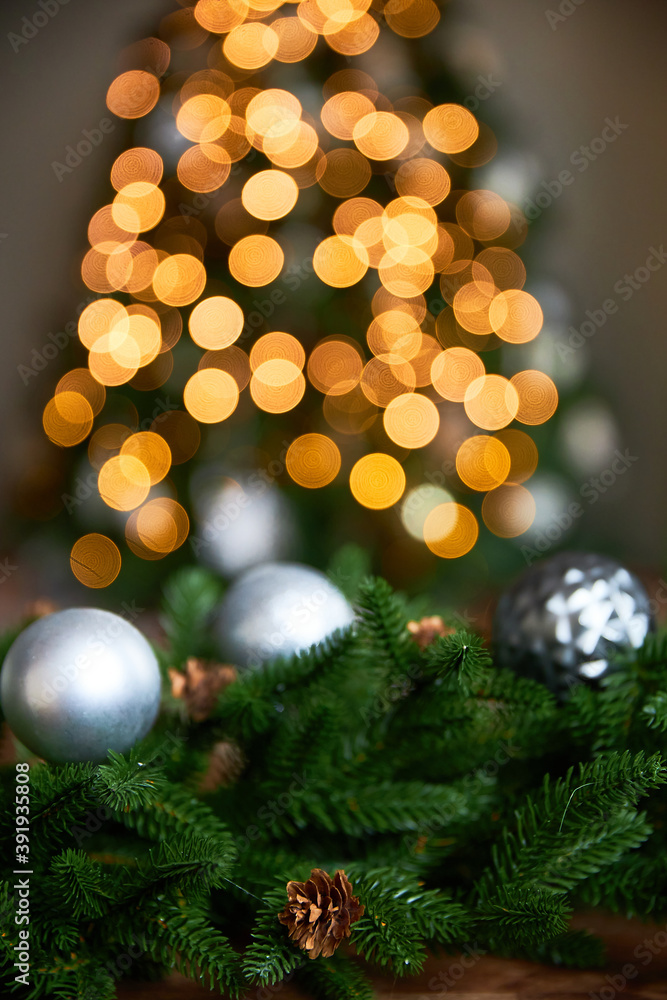 Silver toy for spruce against the background of green spruce and cones and bright garland in the background